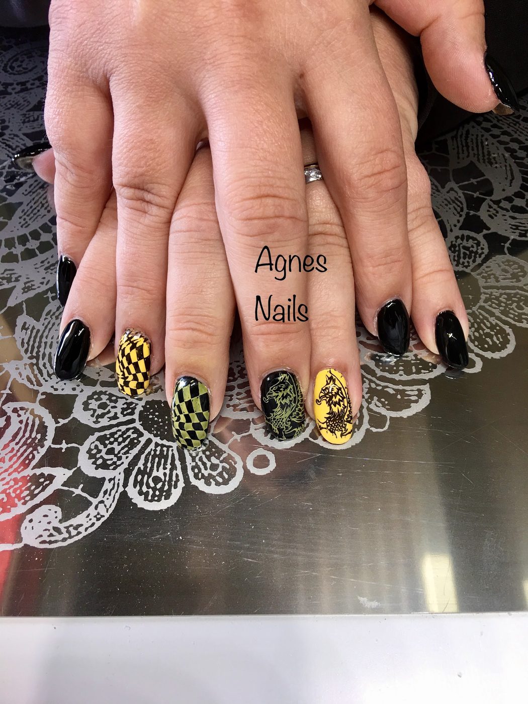 Zwarte nagels met geel-zwart geblokte en beschilderde accentnagels op een kanten onderlegger