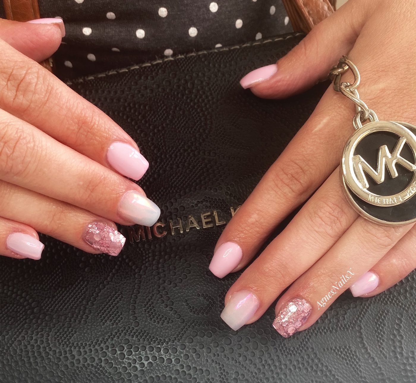 Zachtroze nagels met één glitternagel, hand op een zwarte tas met sleutelhanger