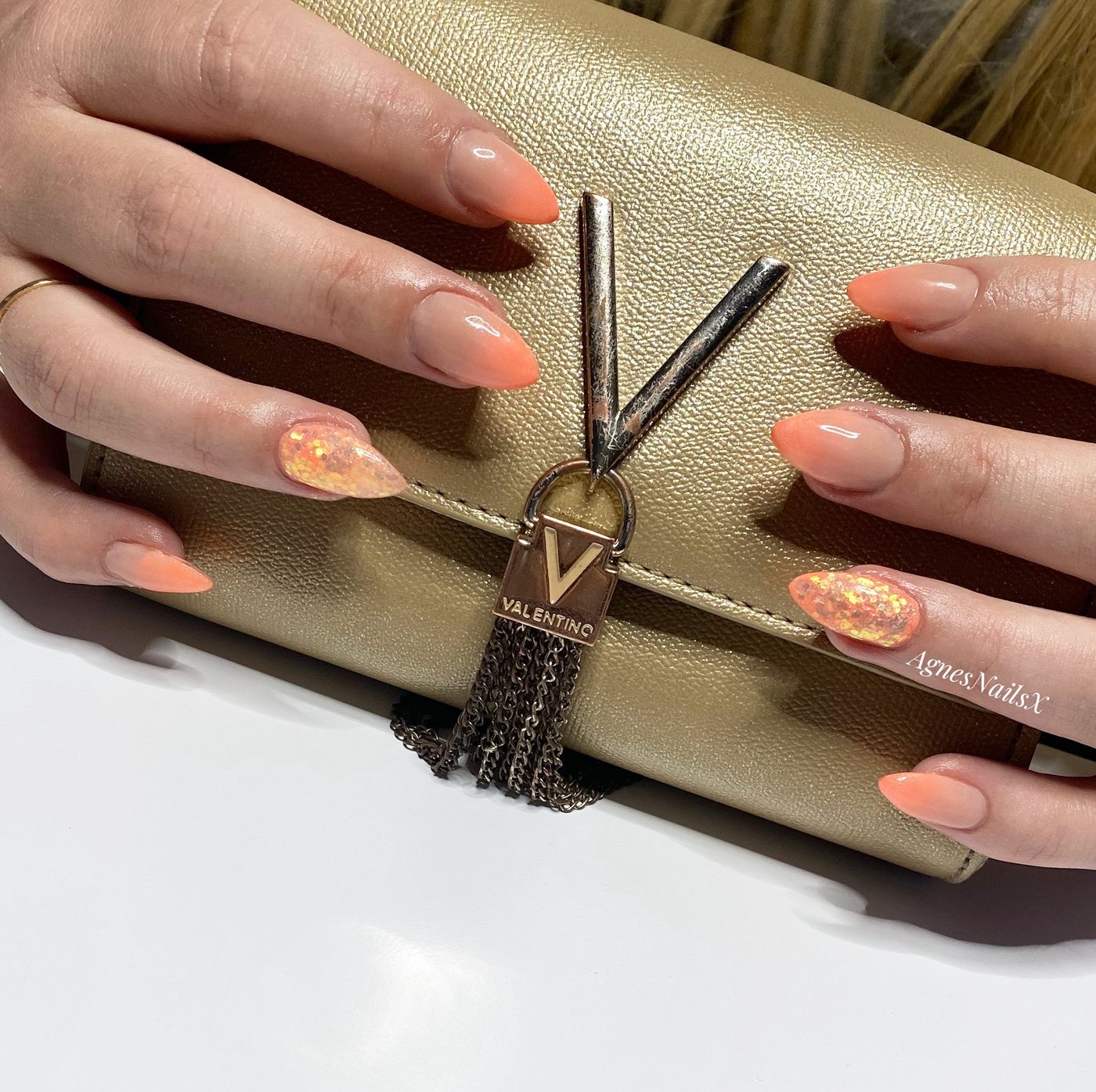 Perzikkleurige amandelnagels met glittervlokken op een gouden tas